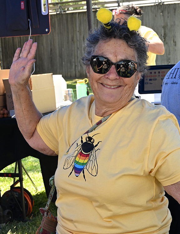 Smiling woman in sunglasses, yellow bee shirt and antenna headband waving outdoors