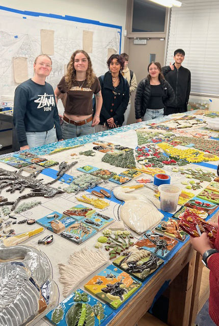 A group of five people stands around a table covered in colorful items and materials.
