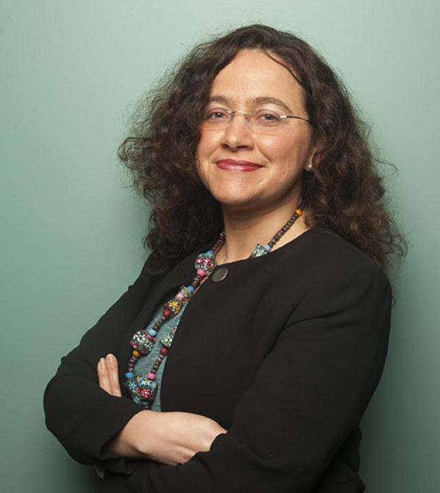 Studio headshot of smiling woman with glasses and curly hair, arms crossed, teal background