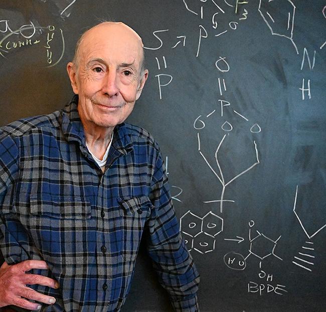 Smiling Bruce Hammock in plaid shirt before chalkboard of chemical formulas