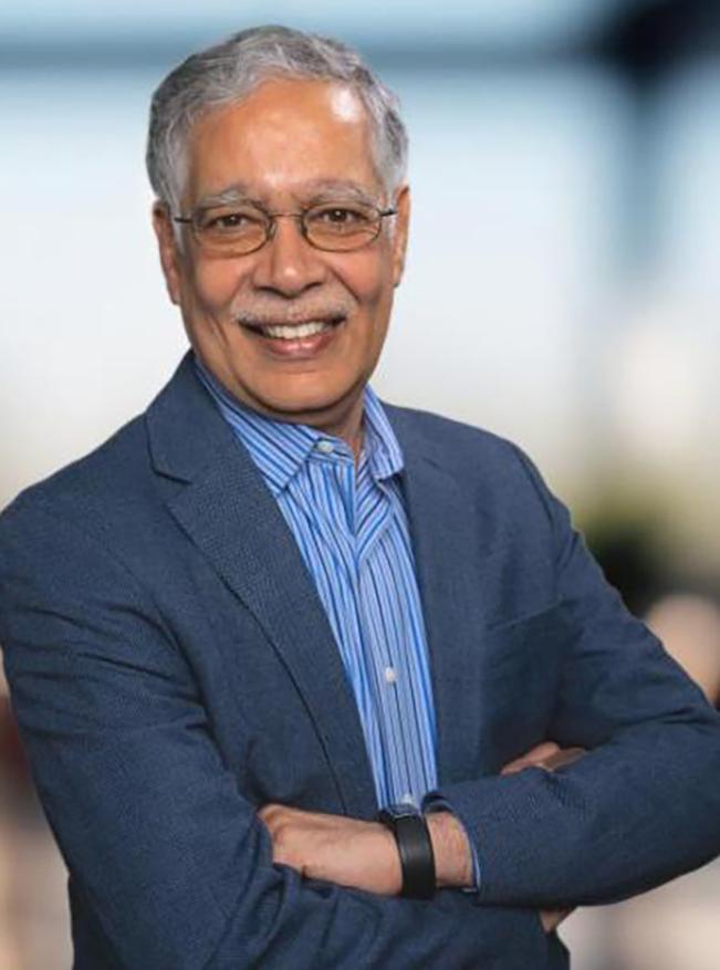 Smiling older man in blue blazer and striped shirt, arms crossed, blurred office background