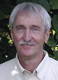 Kenneth Yeargan man with gray hair and mustache wearing light shirt, green leafy background